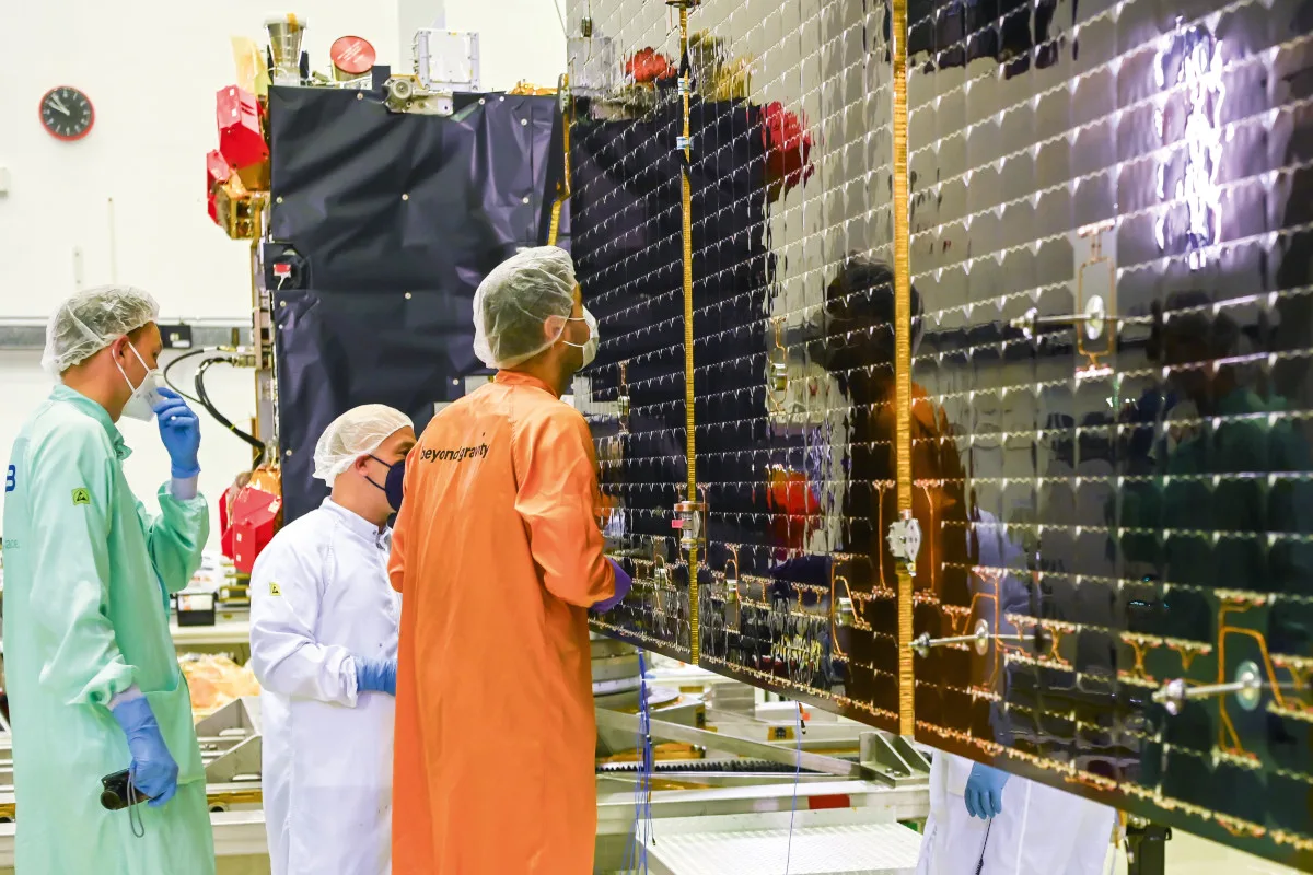 hera_s_wings_of_power_cmyk Three scientists inspecting the solar wings of the Hera spacecraft.