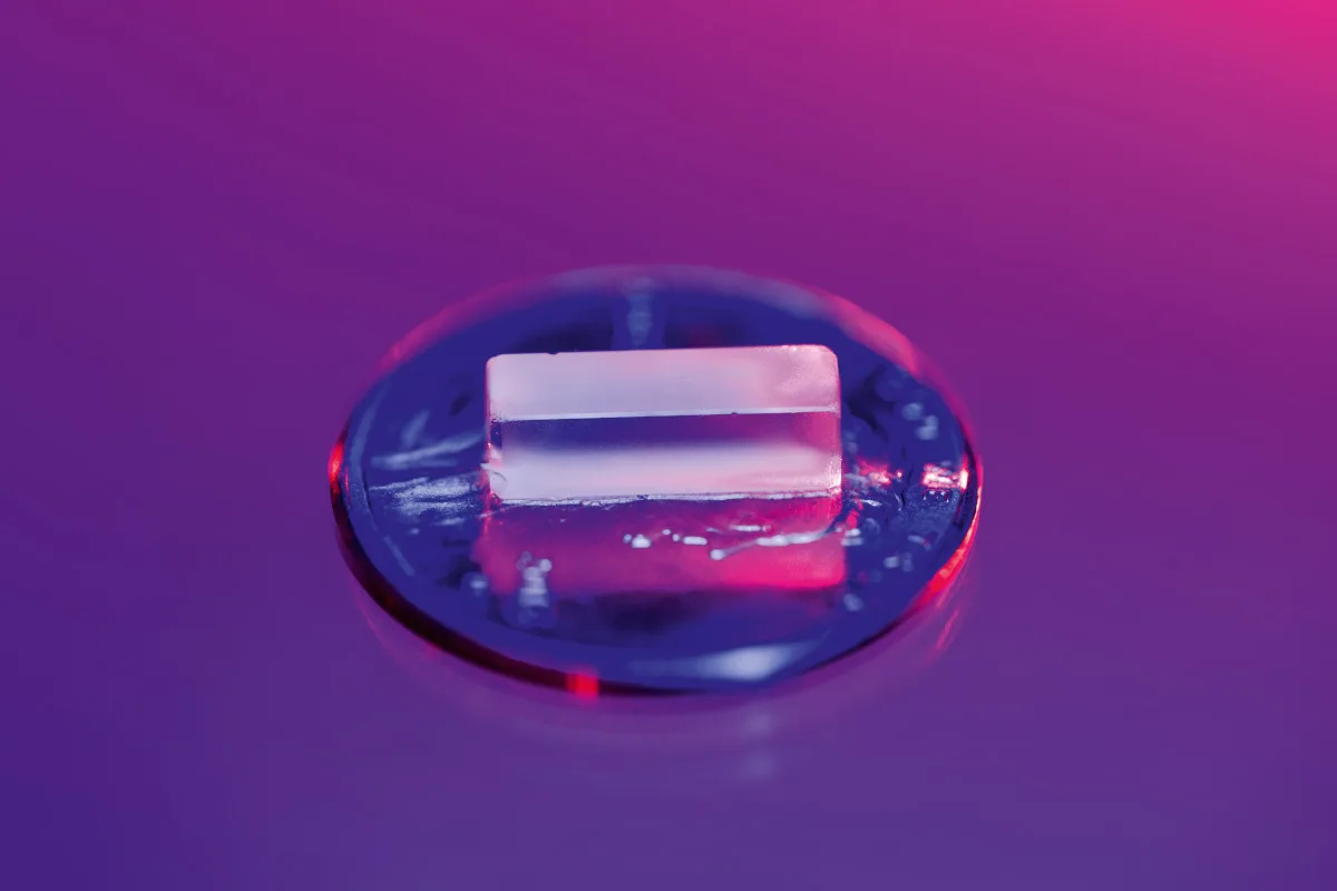 nuclear-clock-crystal A rectangular clear crystal of thorium-229 on top of a shiny disc over a purple background.